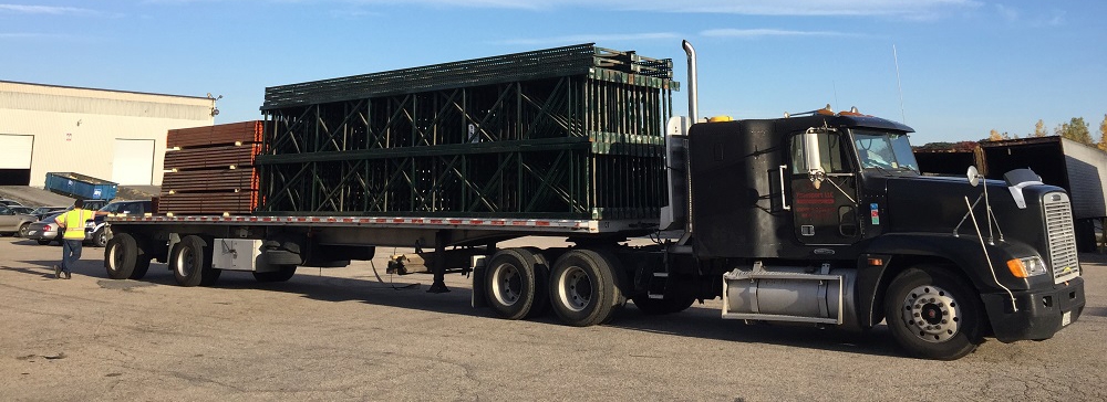 Flatbed truck loaded with used warehouse shelving equipment outside American Surplus facility