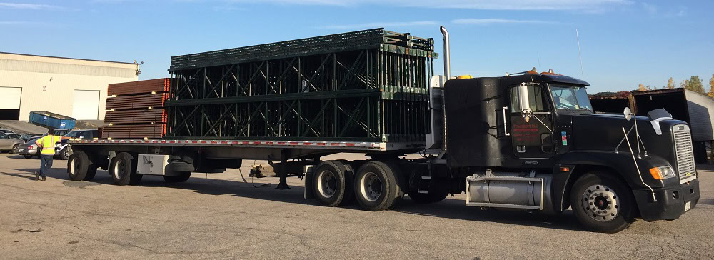 Flatbed truck loaded with used warehouse shelving equipment outside American Surplus facility