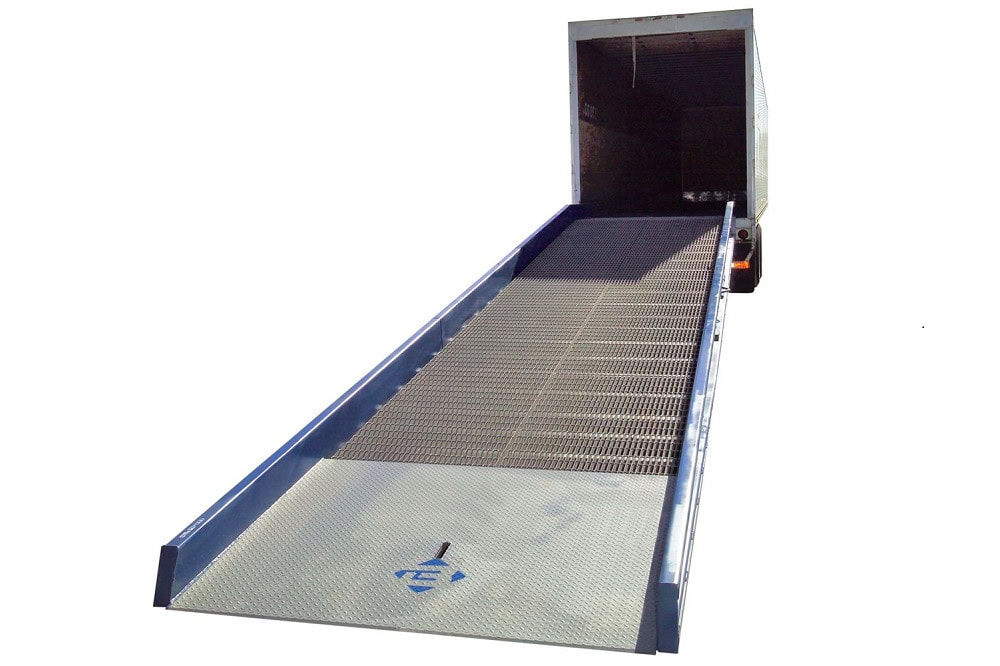 Ground-to-truck yard ramp with bar grate decking and side safety curbs aligned to a semi-trailer for forklift loading and unloading