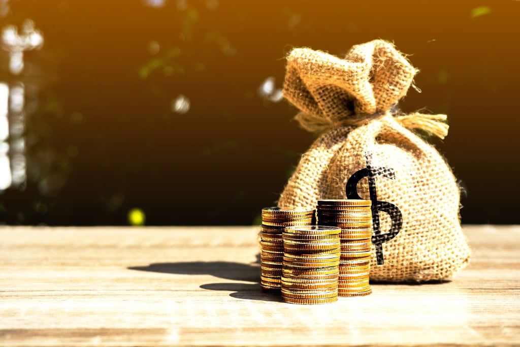 Stacked coins and a burlap money bag with a dollar sign on a wooden table